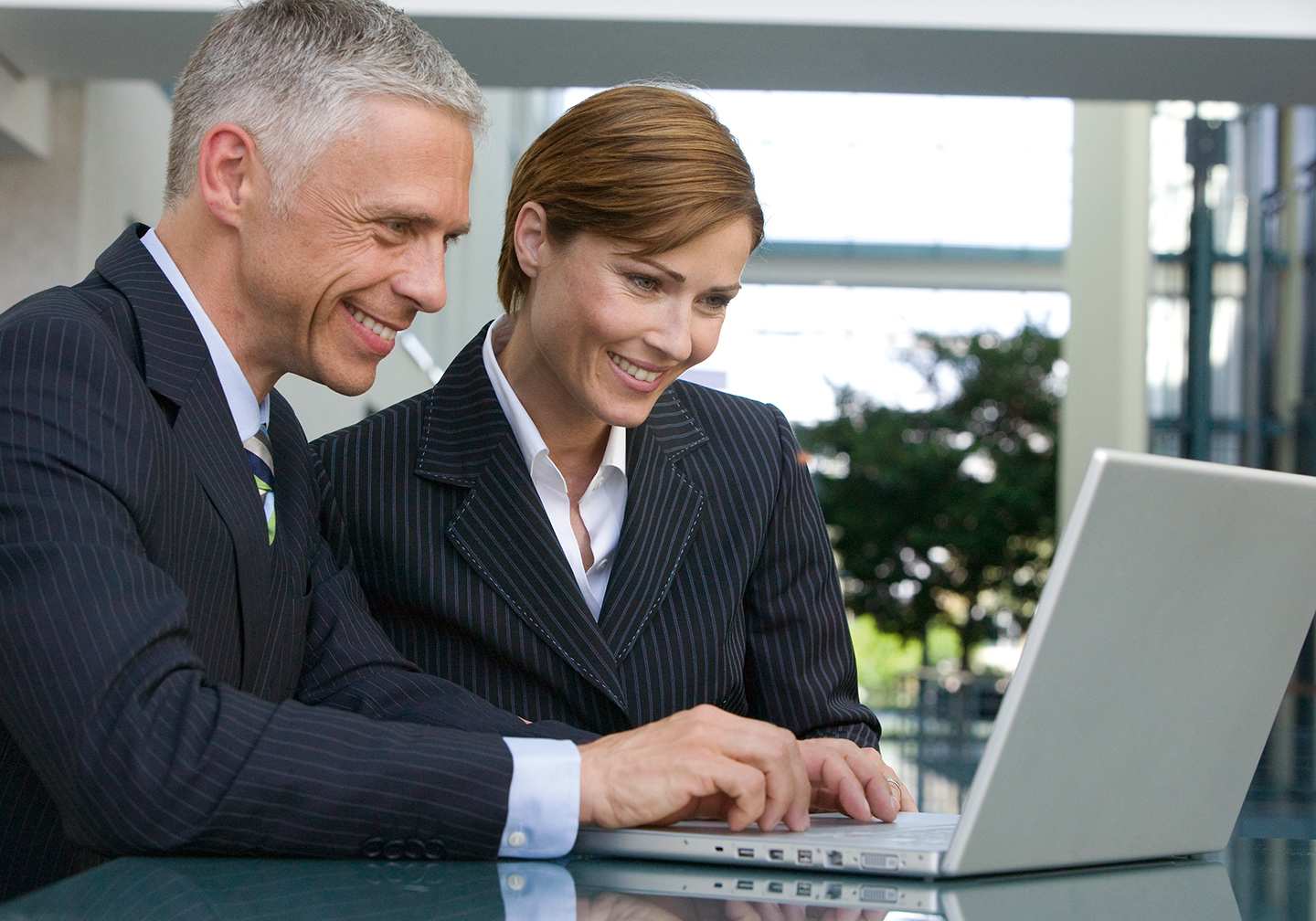 Business-Paar, mittleres Alter, sitzen in Buerogebaeude an Laptop